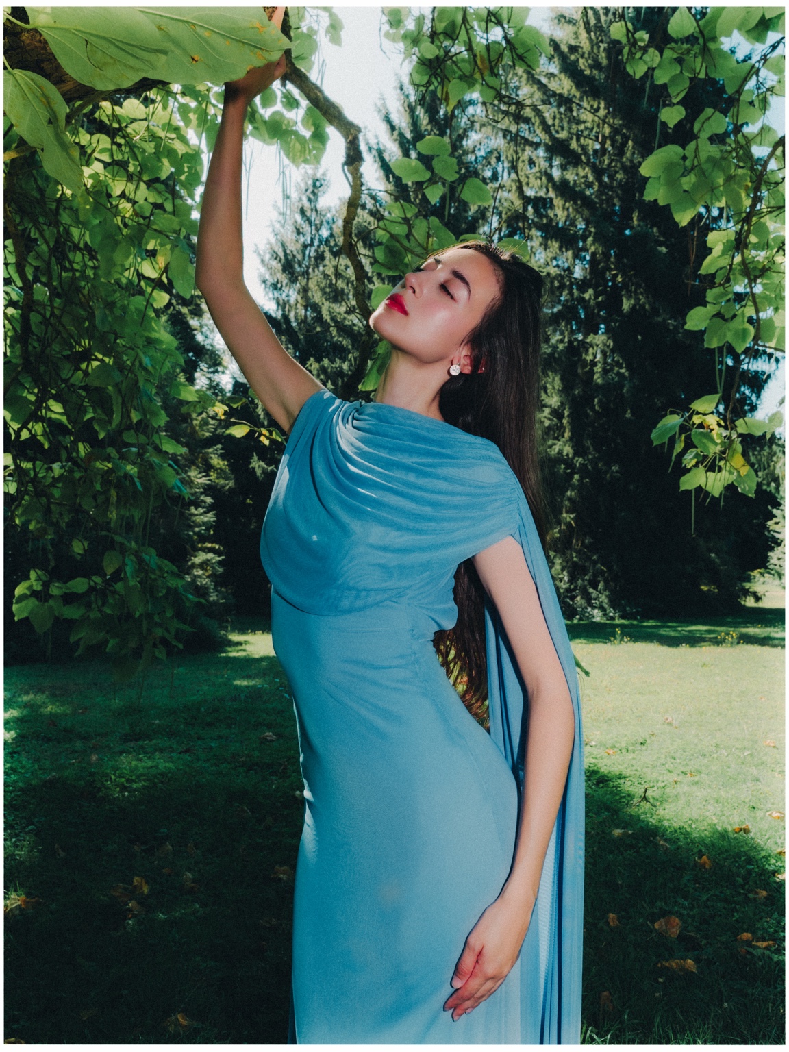 Editorial fashion portrait in a blue dress beneath green foliage